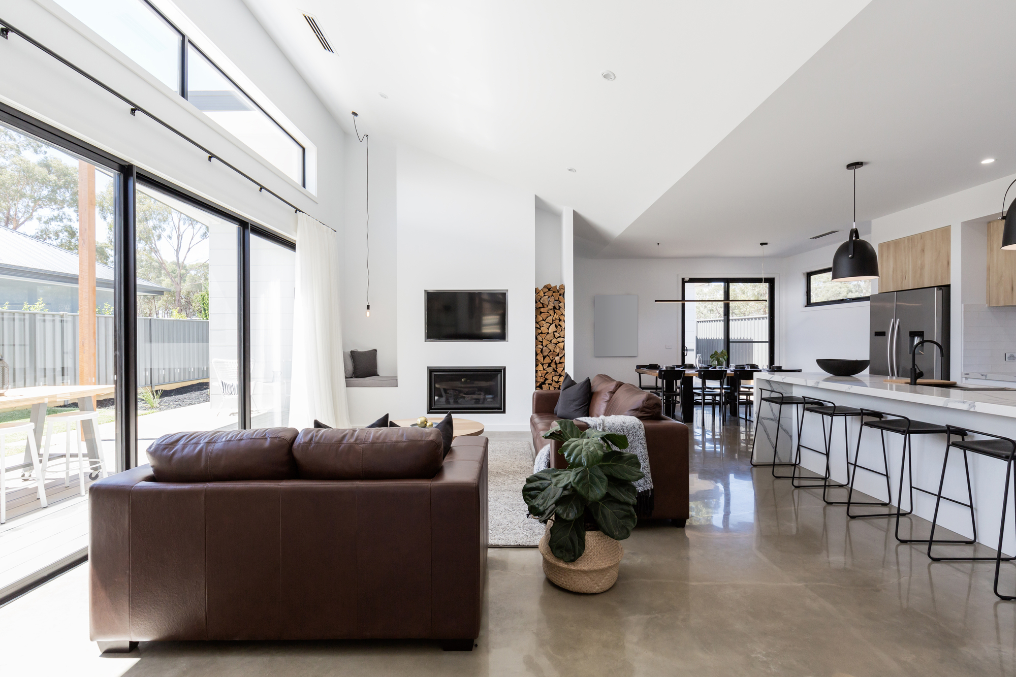 Contemporary open plan living space with polished screed floor, sofas, kitchen, and dining area with table